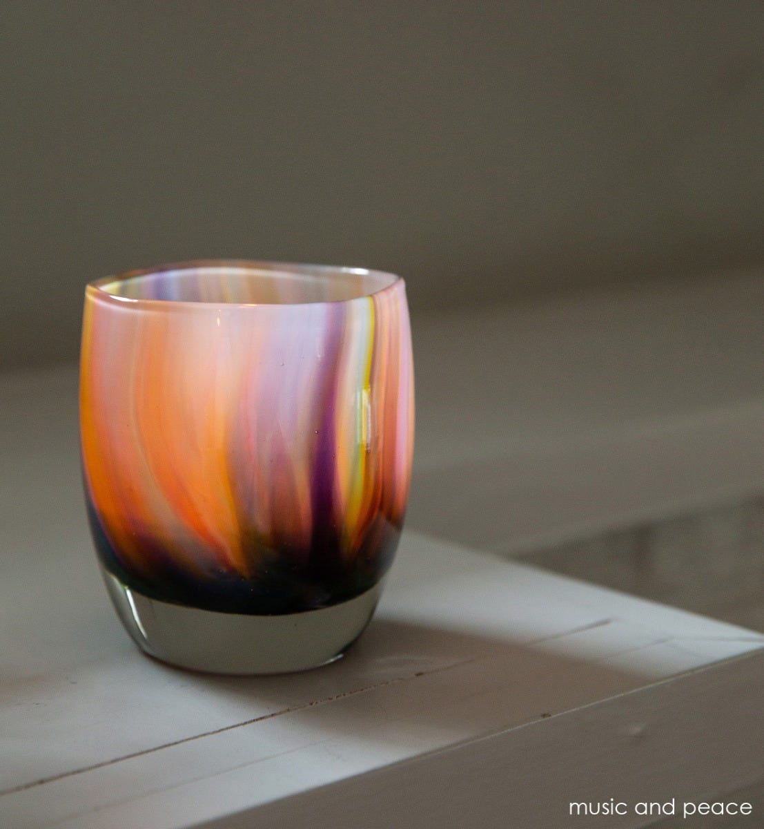 music and peace, rainbow swirled texture, hand-blown glass votive candle holder on a cream surface.