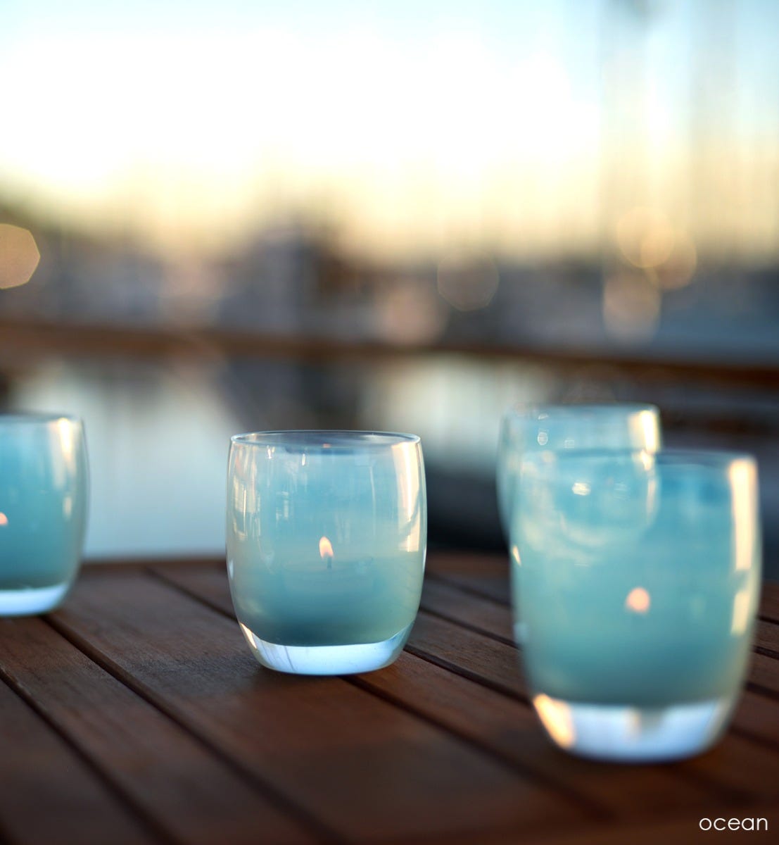 ocean light blue hand-blown glass votive candle holders on an outdoor dark brown patio.