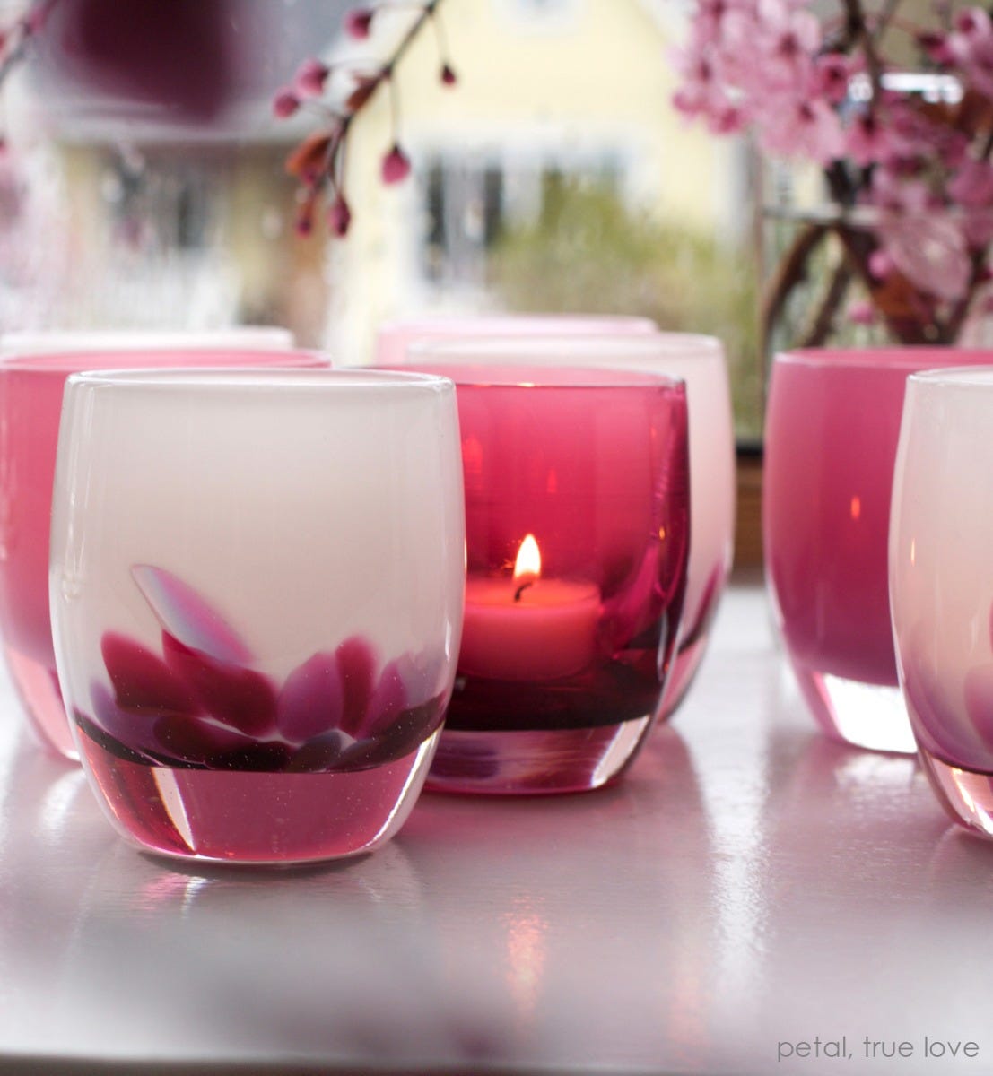 petal, white with pink petals emerging from the bottom, hand-blown glass votive candle holder, paired with true love on a white table with pink flowers in background.