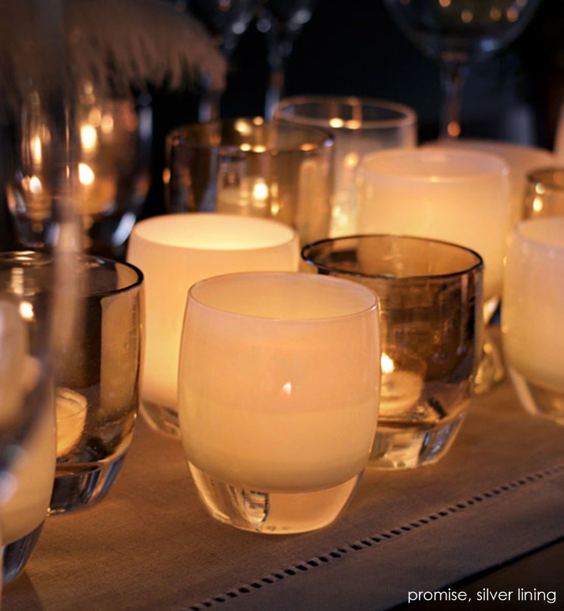 promise cream hand-blown glass votive candle holder lit with silver lining on a dining room table runner.