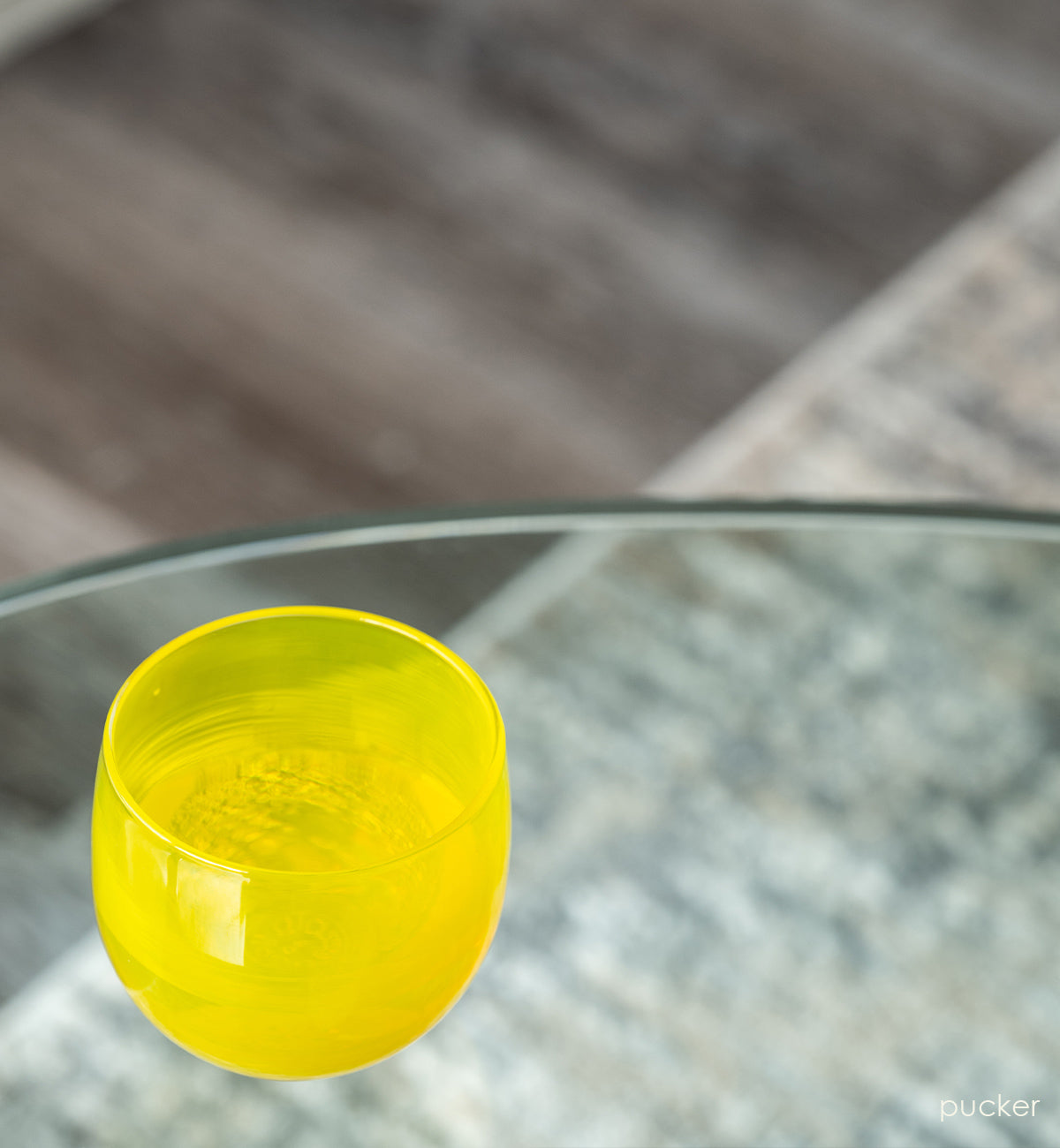 pucker drinker, bright yellow hand-blown drinking glass on a glass coffee table.