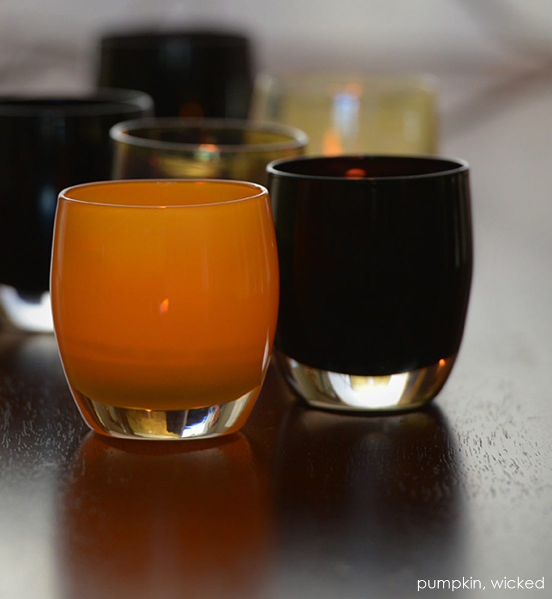 pumpkin orange hand-blown glass votive candle holder with wicked on a dark wood table.