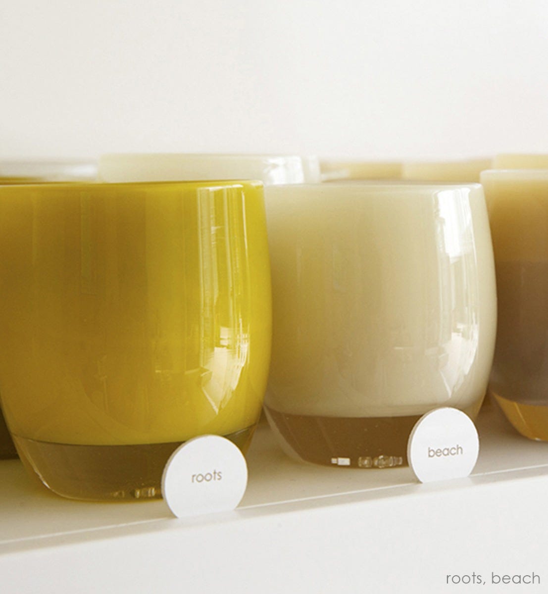roots chartreuse gold hand-blown glass votive candle holder next to beach on a glassybaby shelf.
