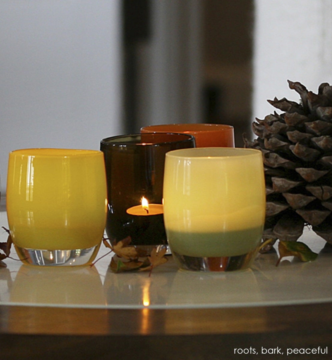 roots chartreuse gold hand-blown glass votive candle holder paired with bark and peaceful on a table with a decorative pinecone.
