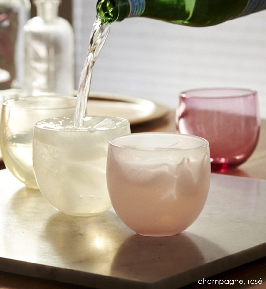 rosé drinker, soft pink hand-blown drinking glass with champagne drinker on a marble tray, with bubbly water being poured into them.