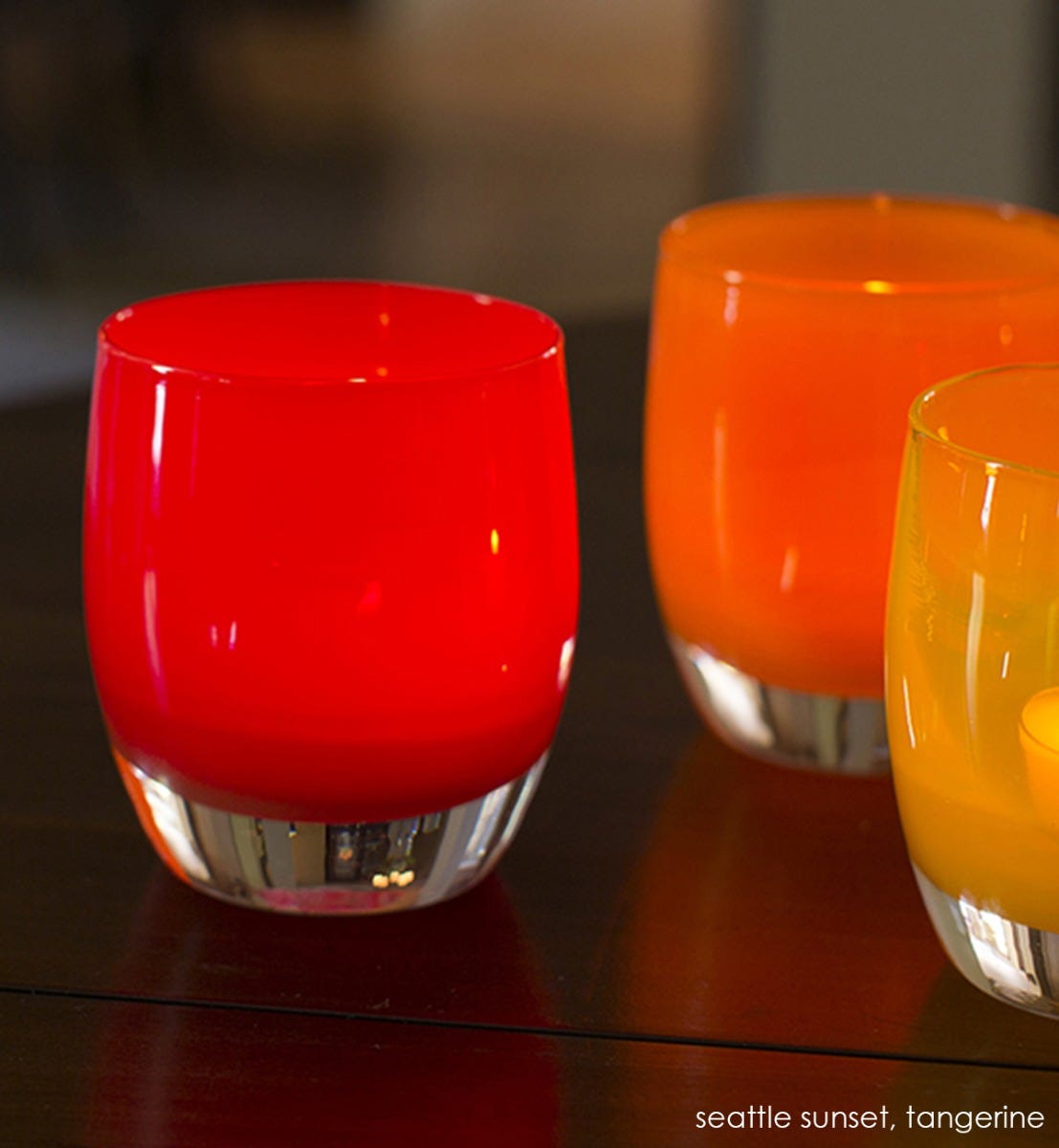 seattle sunset, bright orange red, hand-blown glass votive candle holder with tangerine on a circular wood table.
