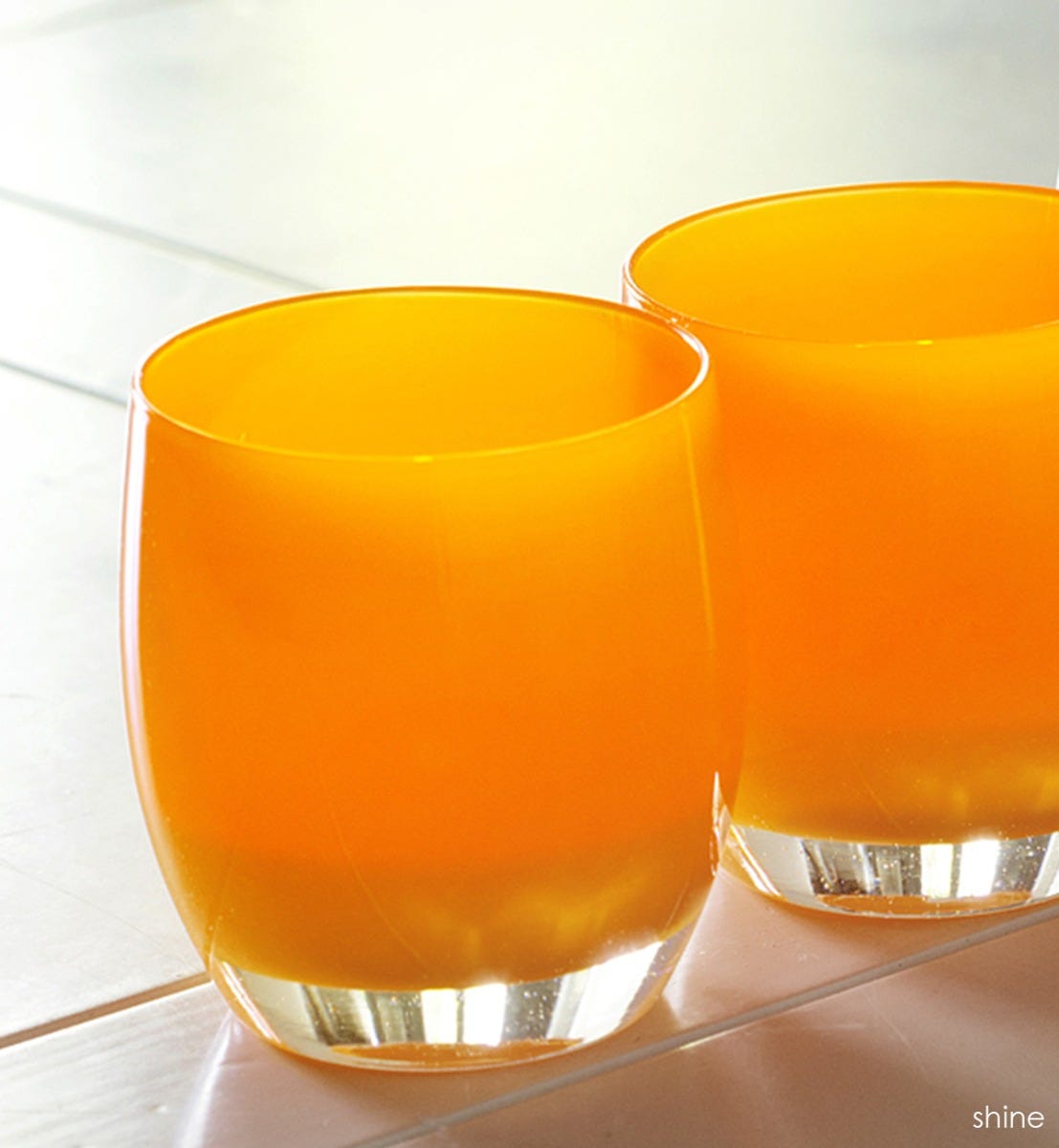 two shine hand-blown bright orange glass votive candle holders on a cream tiled table.