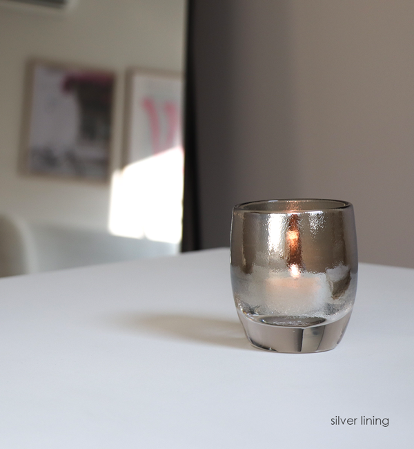silver lining, chrome topped clear, hand-blown glass votive candle holder on a white table with mirror in background.