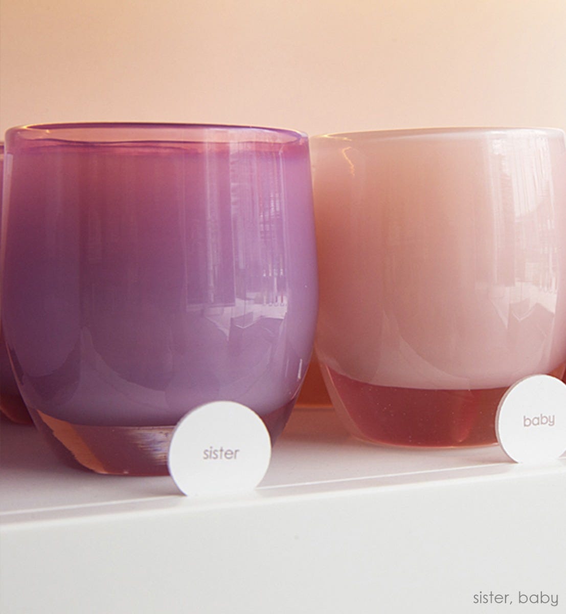 sister mauve purple hand-blown glass votive candle holder on a glassybaby shelf next to a light pink baby.