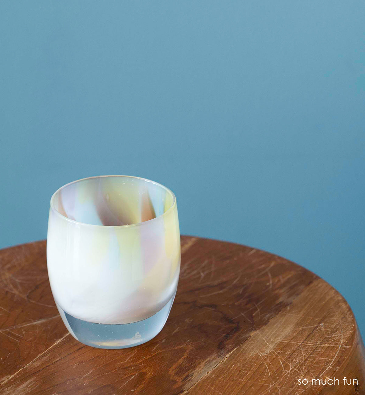 so much fun, pastel mix, hand-blown glass votive candle holder on a wood circular table with blue background.
