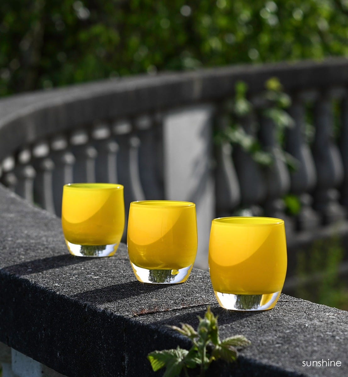 three sunshine, opaque yellow, hand-blown glass votive candle holders on a concrete wall outside.