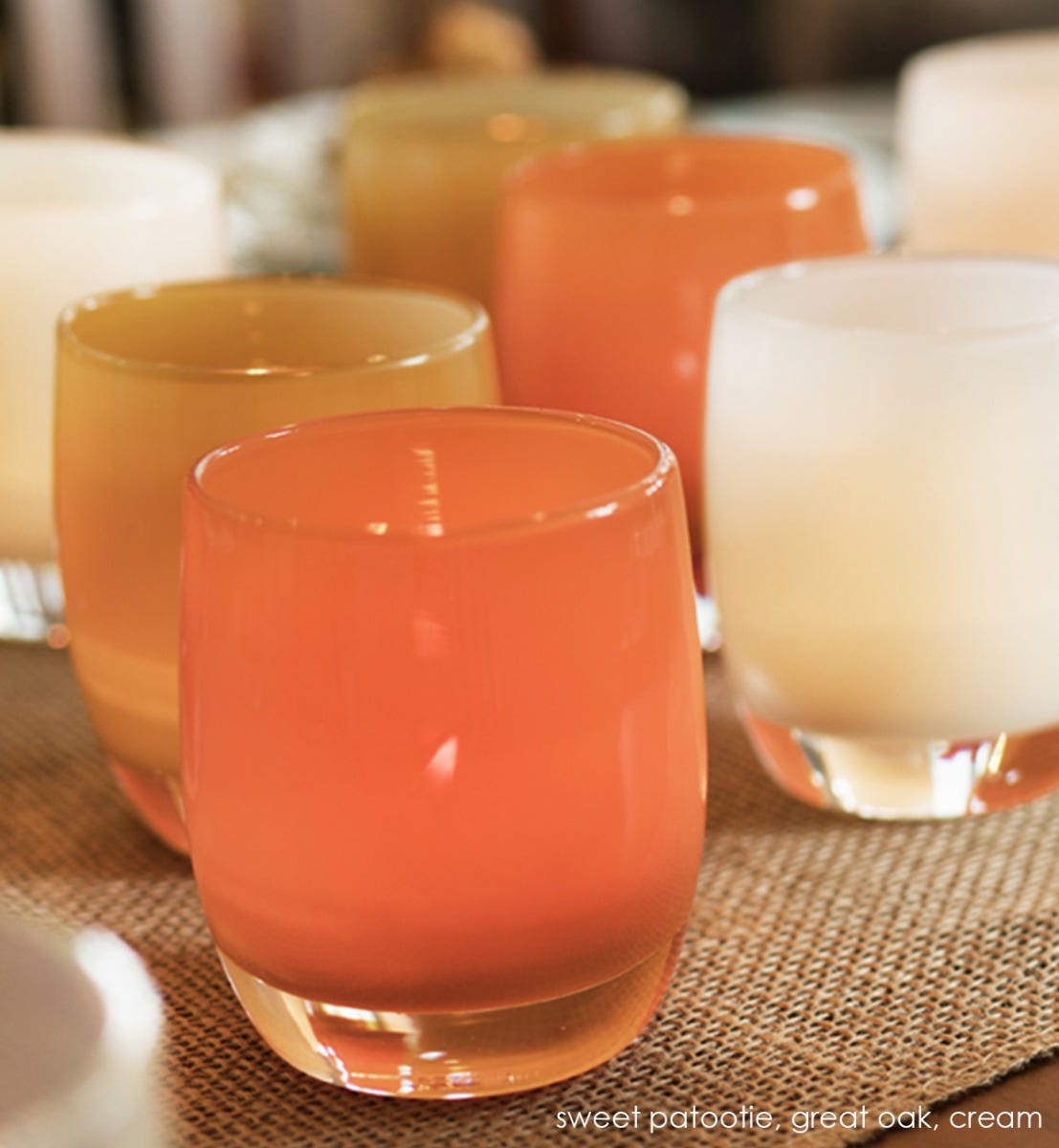 two sweet patootie, apricot orange, hand-blown glass votive candle holders with great oak and cream on a dining table runner.