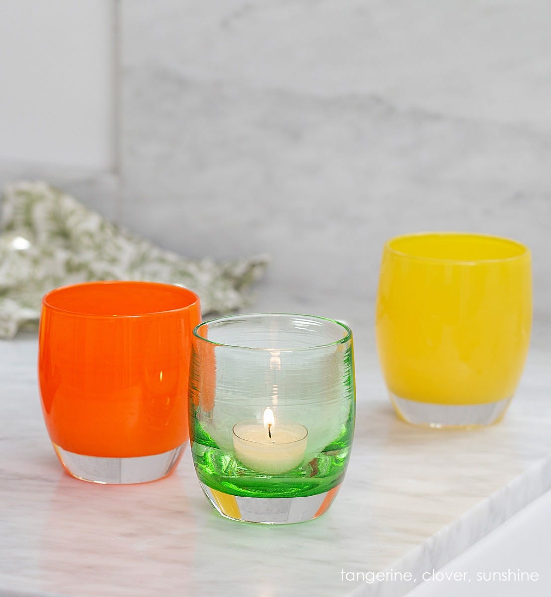 tangerine orange hand-blown glass votive candle holder. Paired with clover and sunshine on a marble counter.
