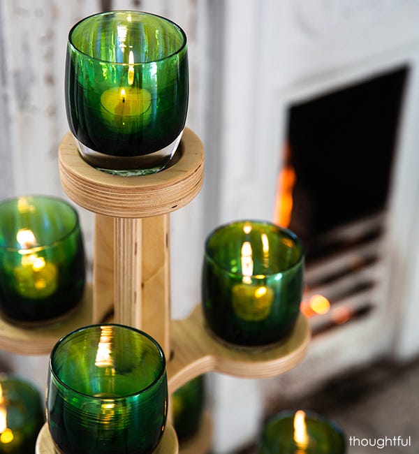several thoughtful deep green with silver metallic interior, hand-blown glass votive candle holders on a glassybaby tree in front of white walls and dark fireplace.