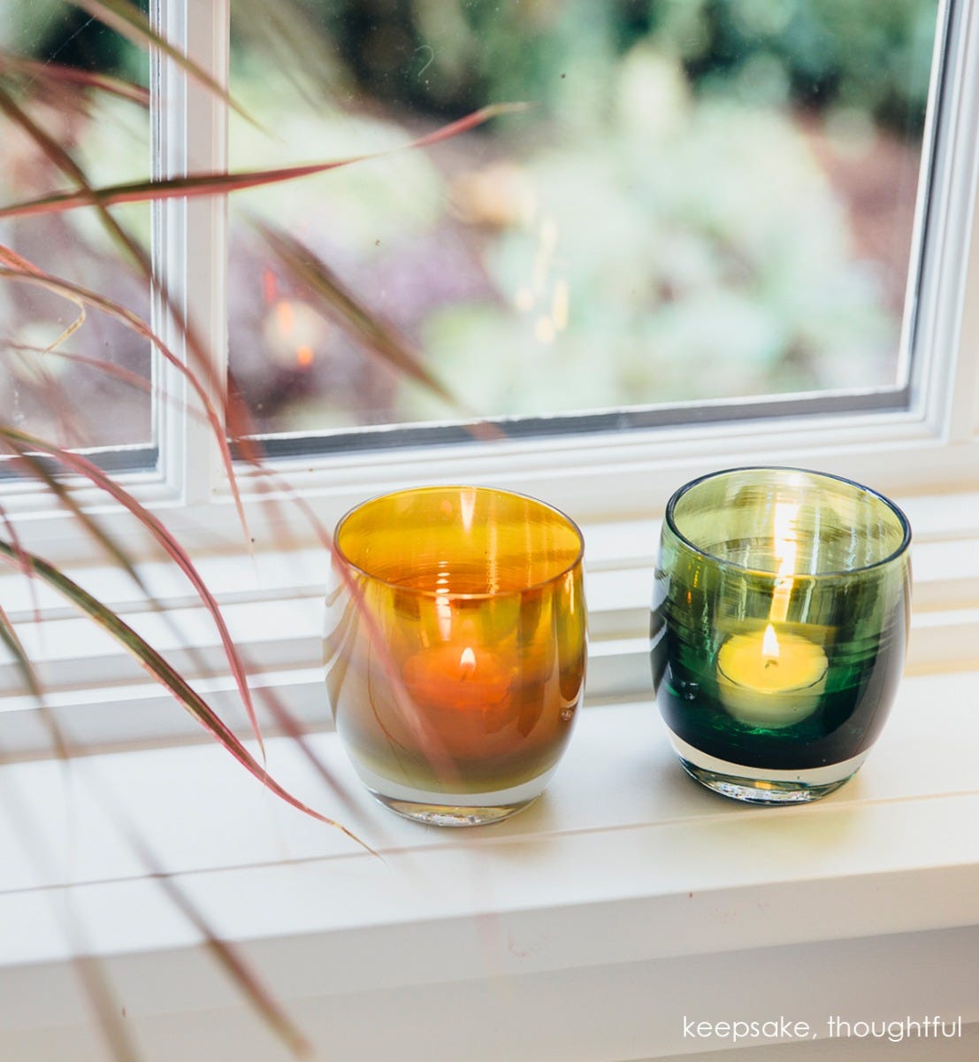 thoughtful deep green with silver metallic interior, hand-blown glass votive candle holder. Paired with keepsake on a white windowsill.