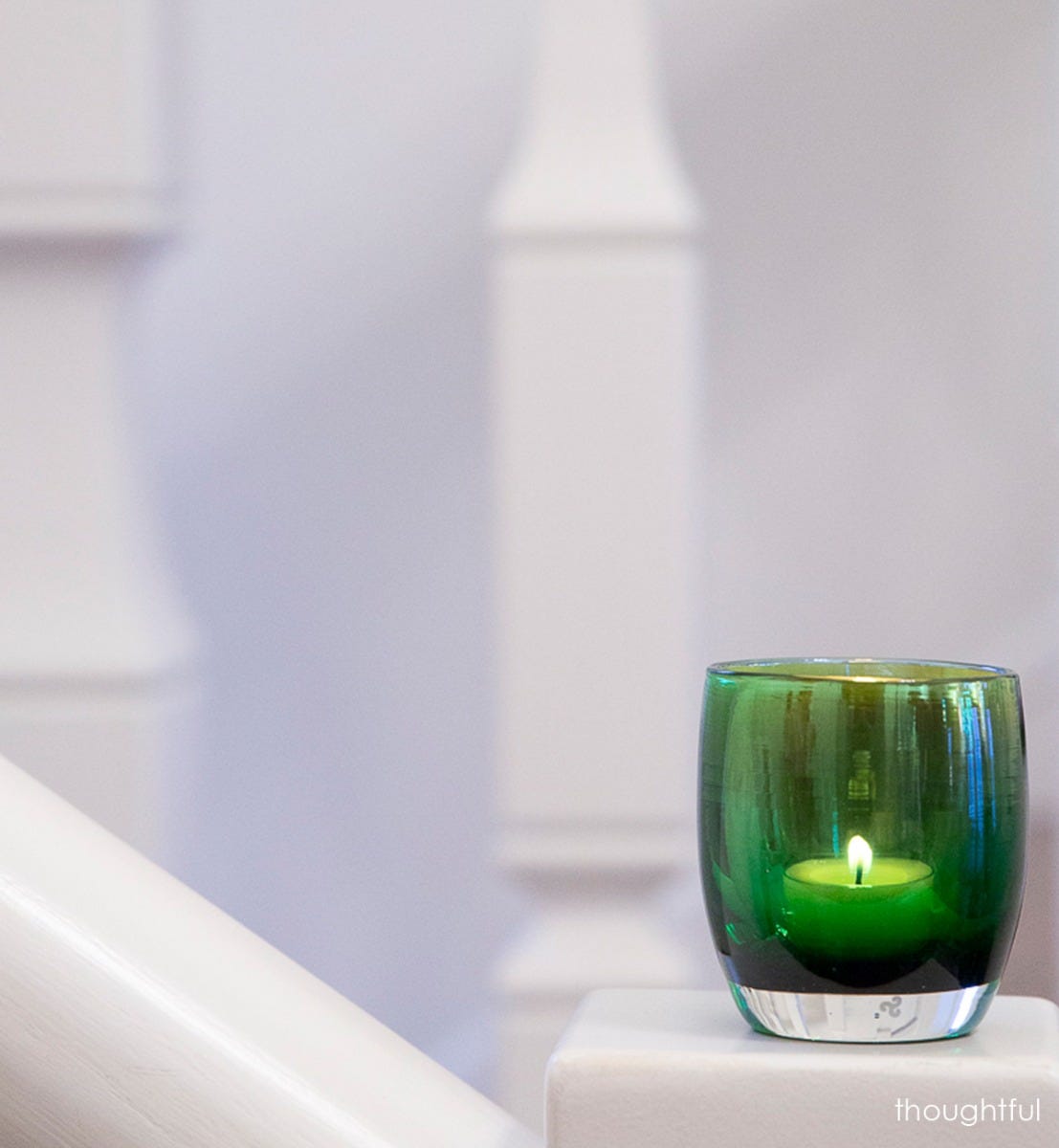 thoughtful deep green with silver metallic interior, hand-blown glass votive candle holder perched on a staircase pillar.