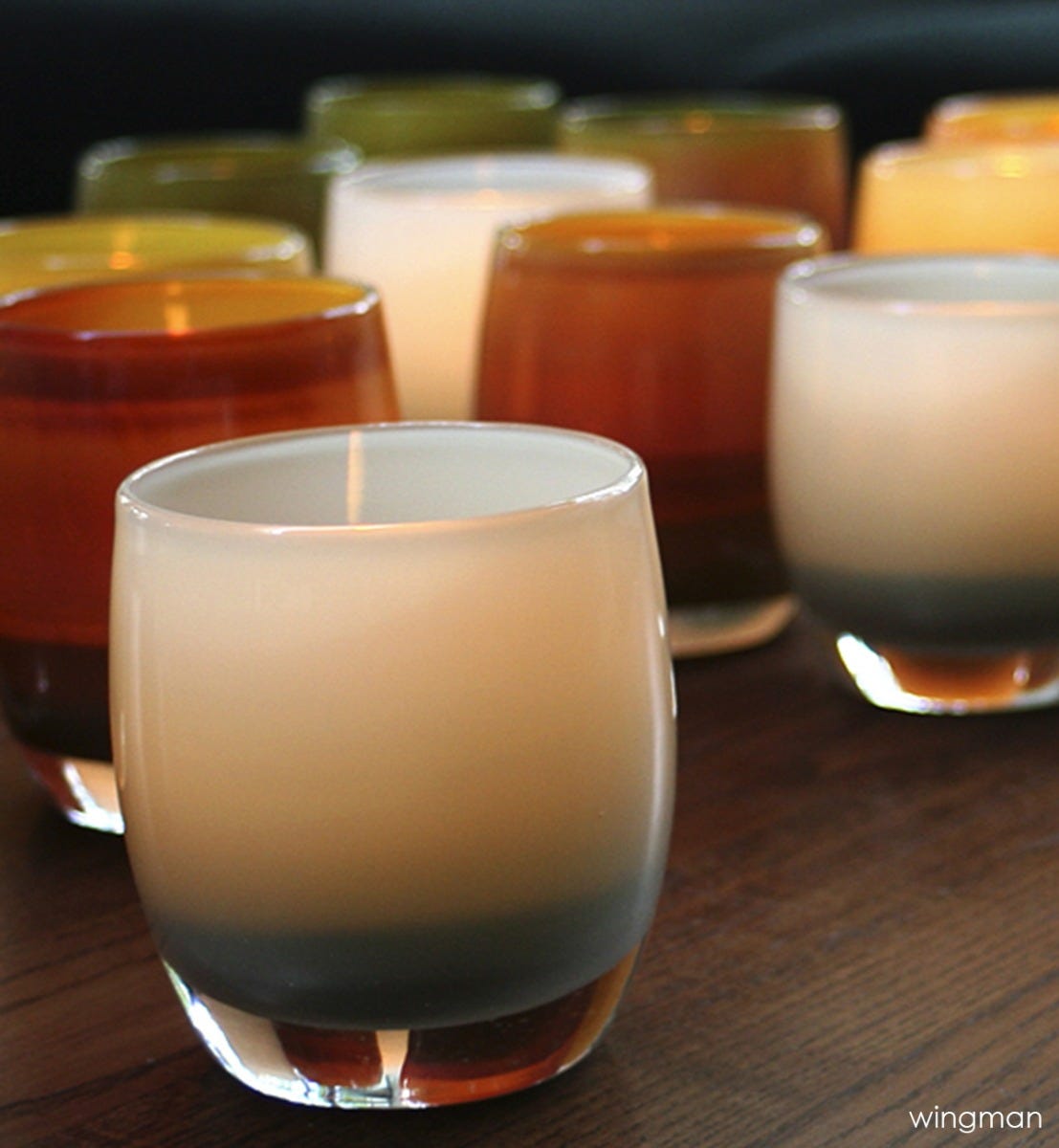 two wingman, harbor gray, hand-blown glass votive candle holders on a dark wood surface with other glassybaby.