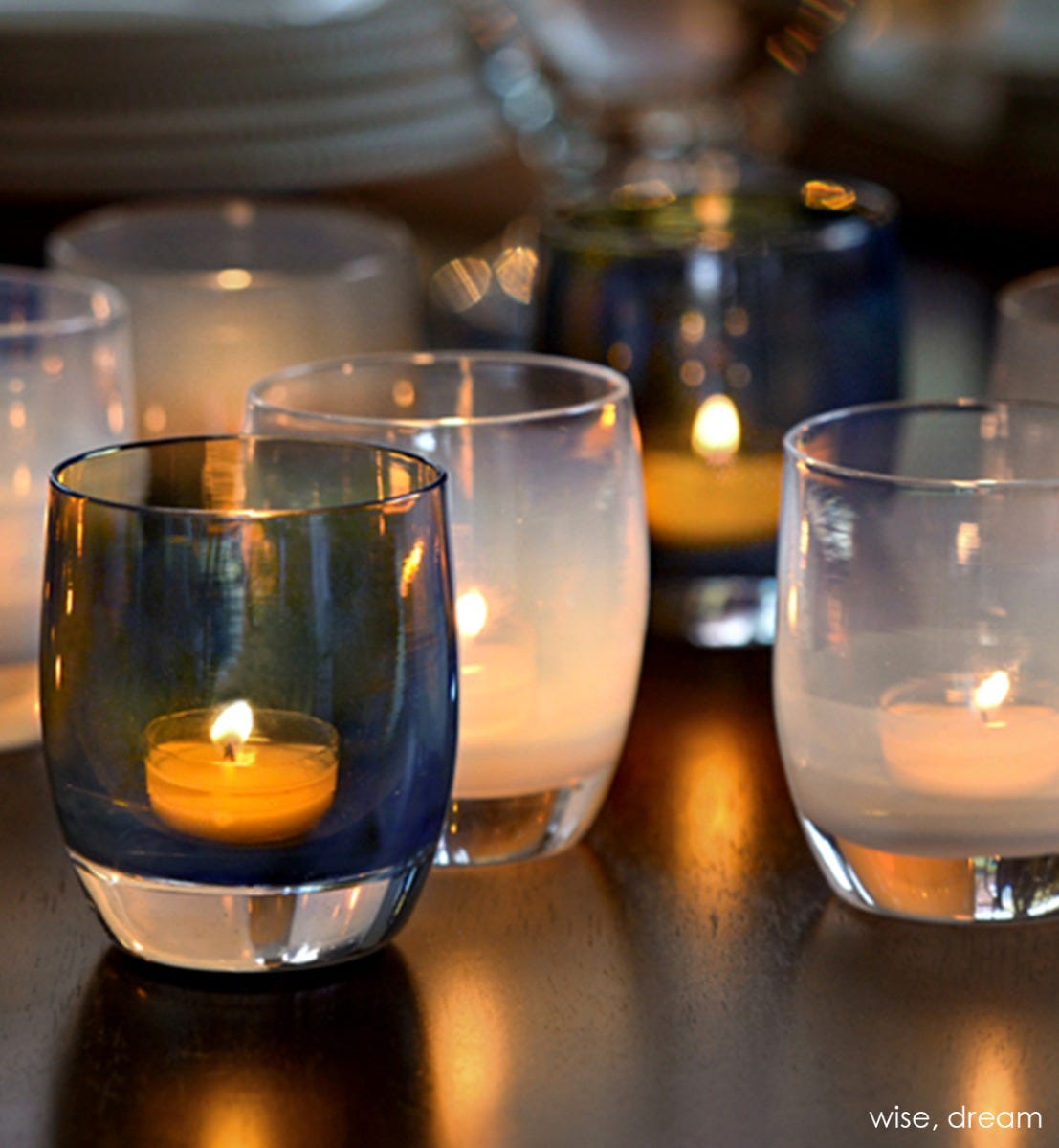 two wise translucent deep gray with wisps of purple and yellow hand-blown glass votive candle holders. Paired with dream on a dark surface with plates in background.