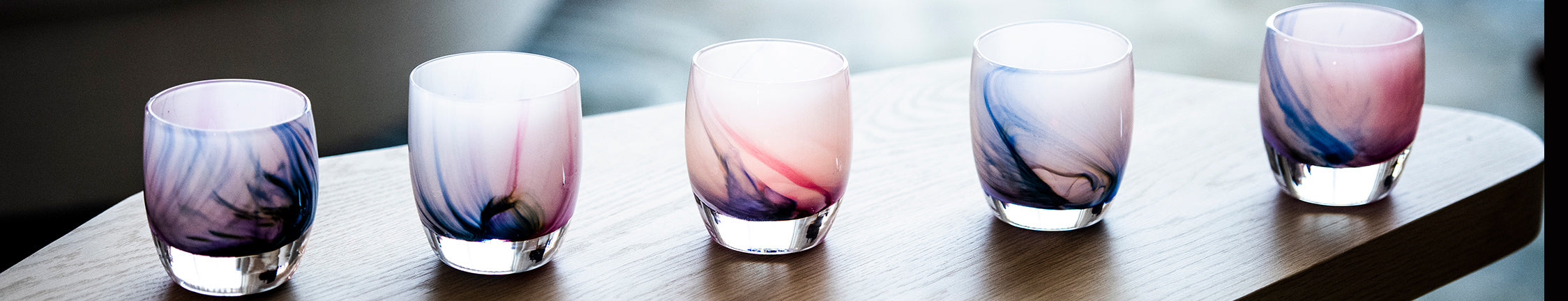 five eye of the storm, lavish blue, purple, blue and pink swirled hand-blown glass votive candle holders on a wood coffee table.