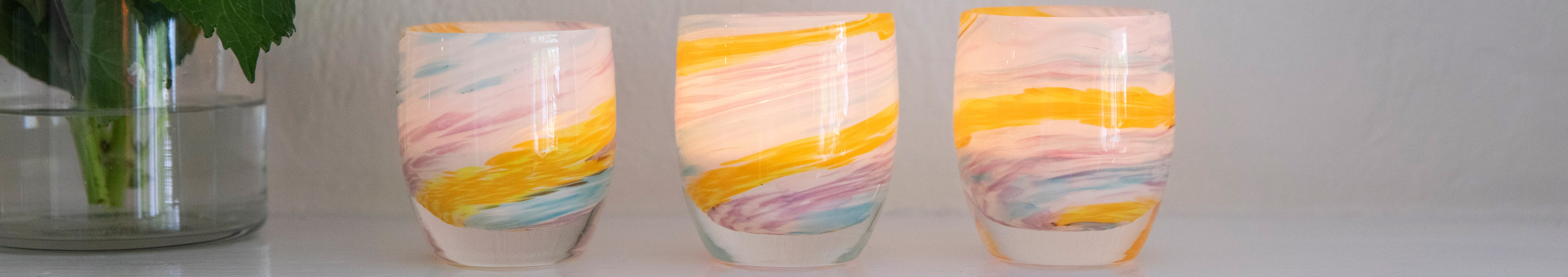 places you'll go, treasure multi-swirl yellow, white, blue, purple hand-blown glass votive candle holders on a mantle next to a vase.