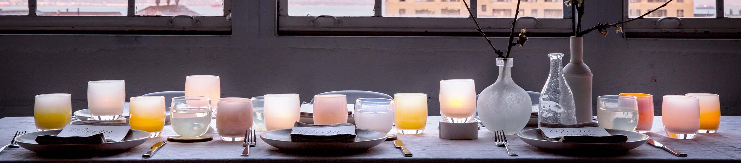 table set with hand-blown glass votive candle holders, illuminated by the sunset on a bay.