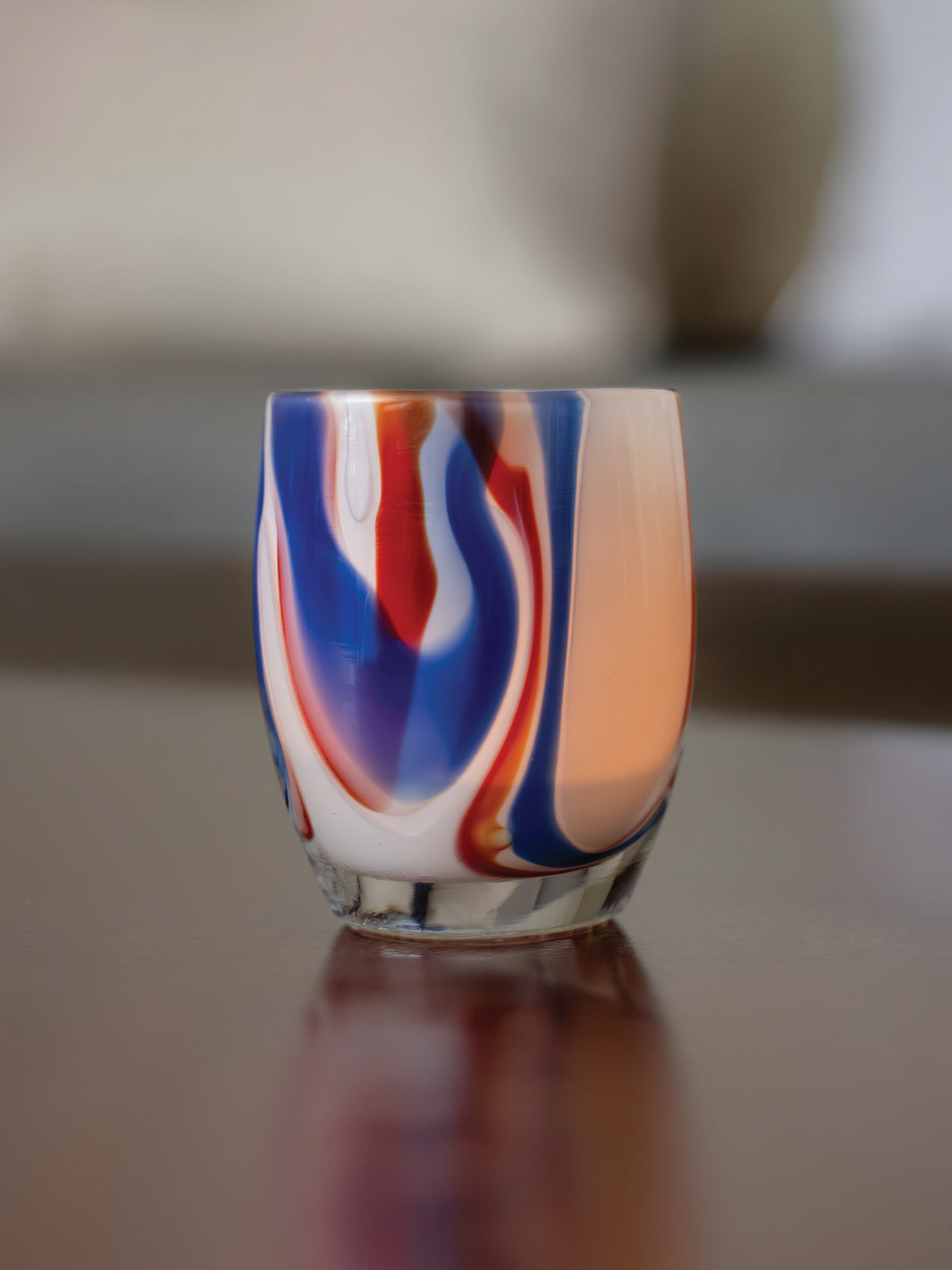 250th, red white and blue swirl glass candle holder on a reflective surface with a blurred background