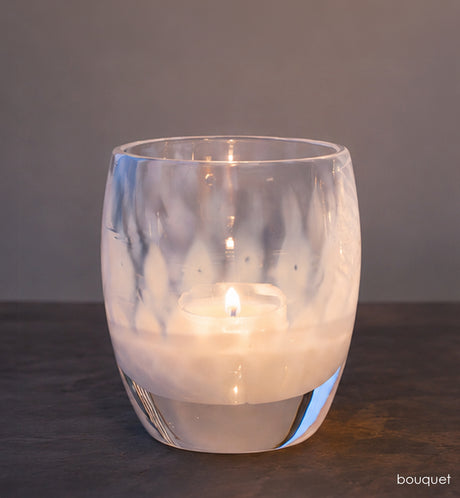 Clear glass candle holder with a lit candle on a dark surface and gray background
