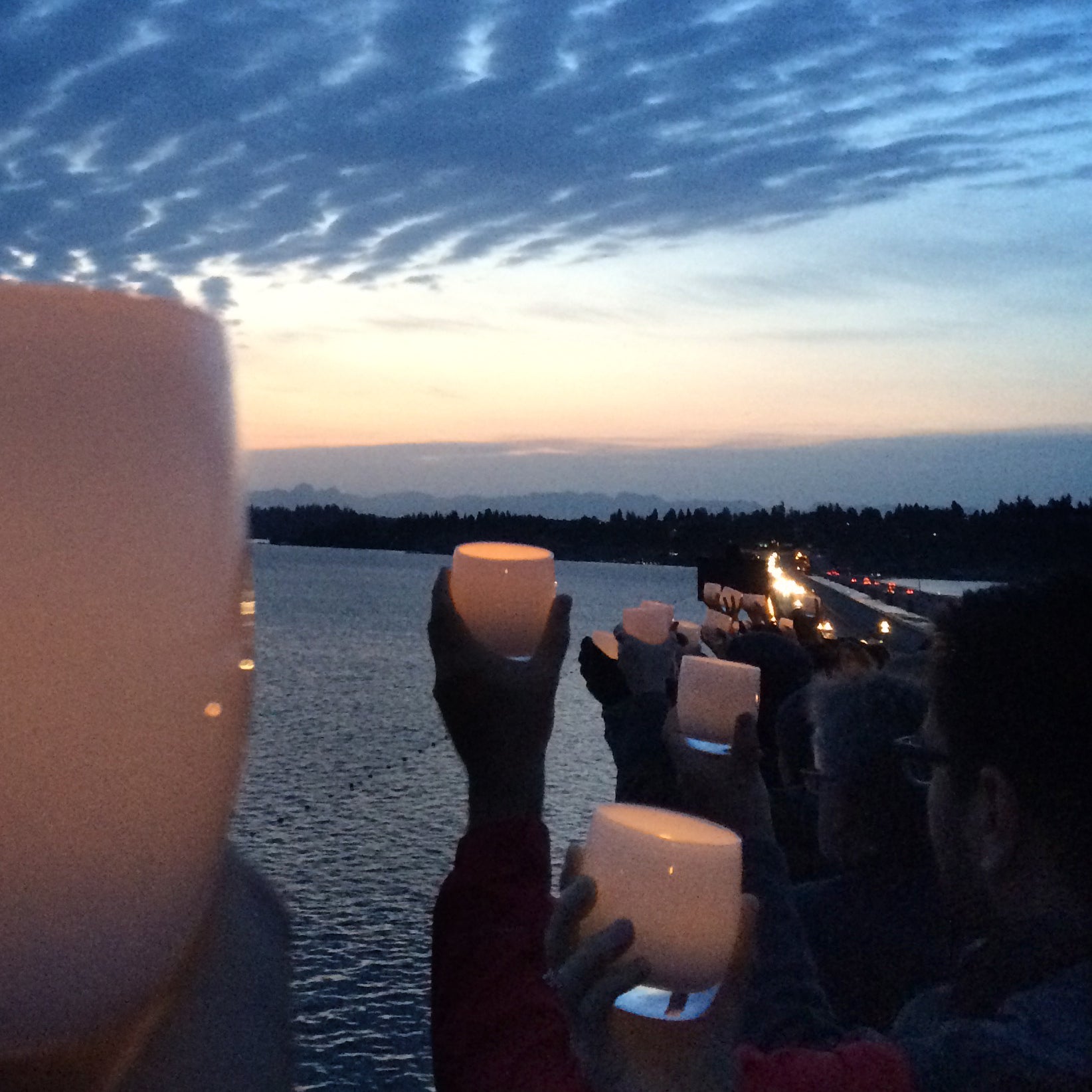 hope white hand-blown candle holder, being held while lit by many people over lake