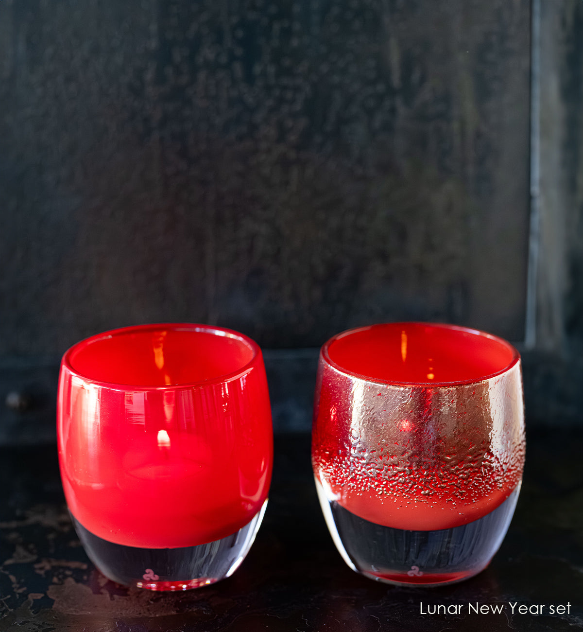 Two red candles in glass candle holders on a dark background
