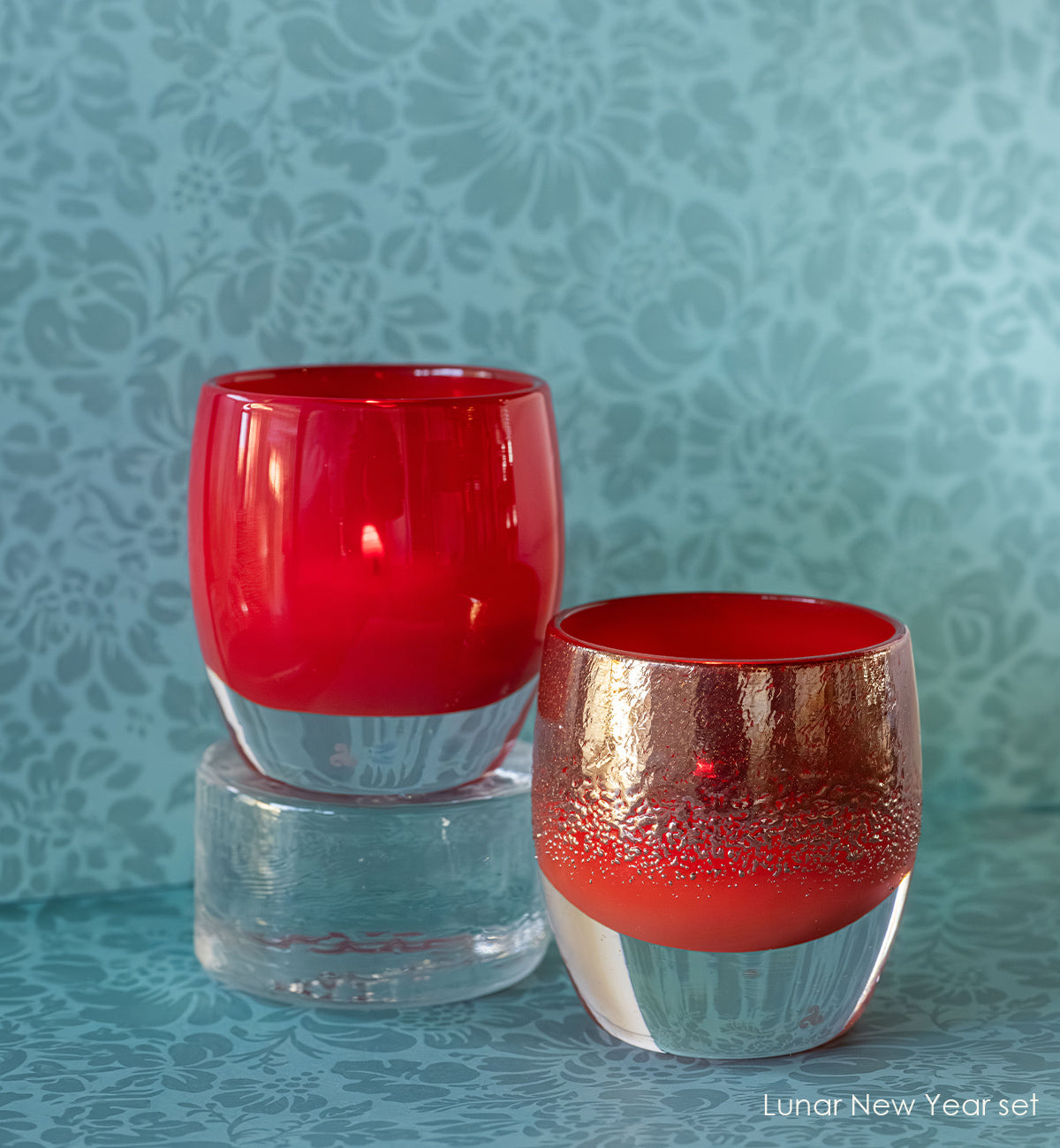 Two red and gold glass candle holders on a textured blue background