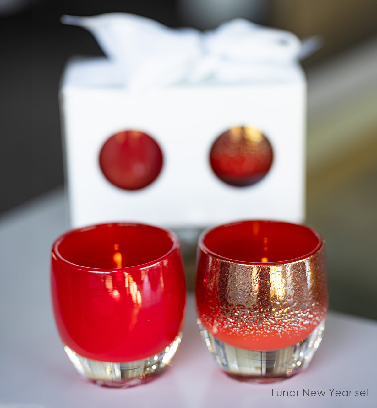 Two red and gold candle holders with a blurred gift box in the background.