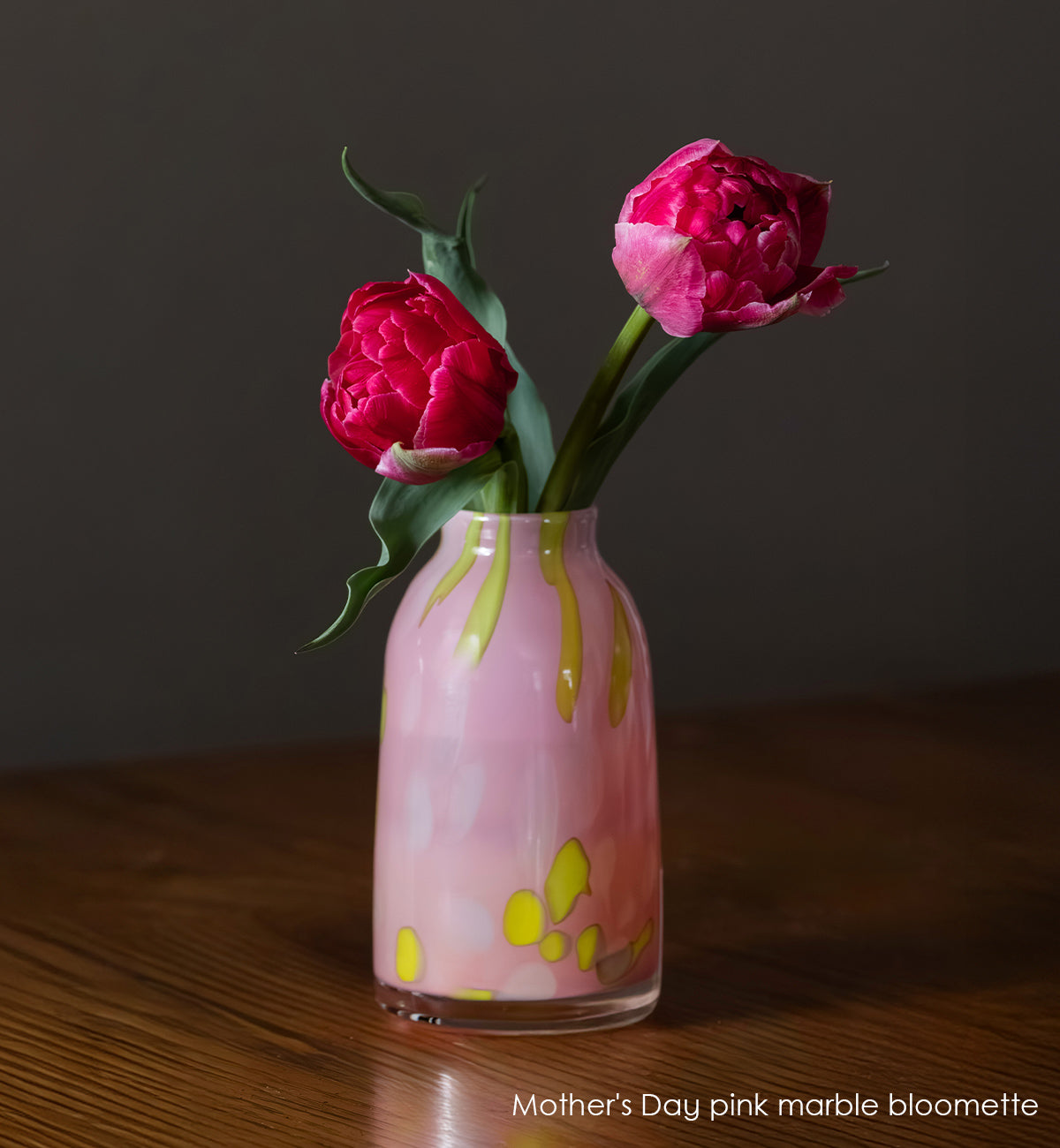 Pink marble-patterned vase with two pink flowers on a wooden surface.