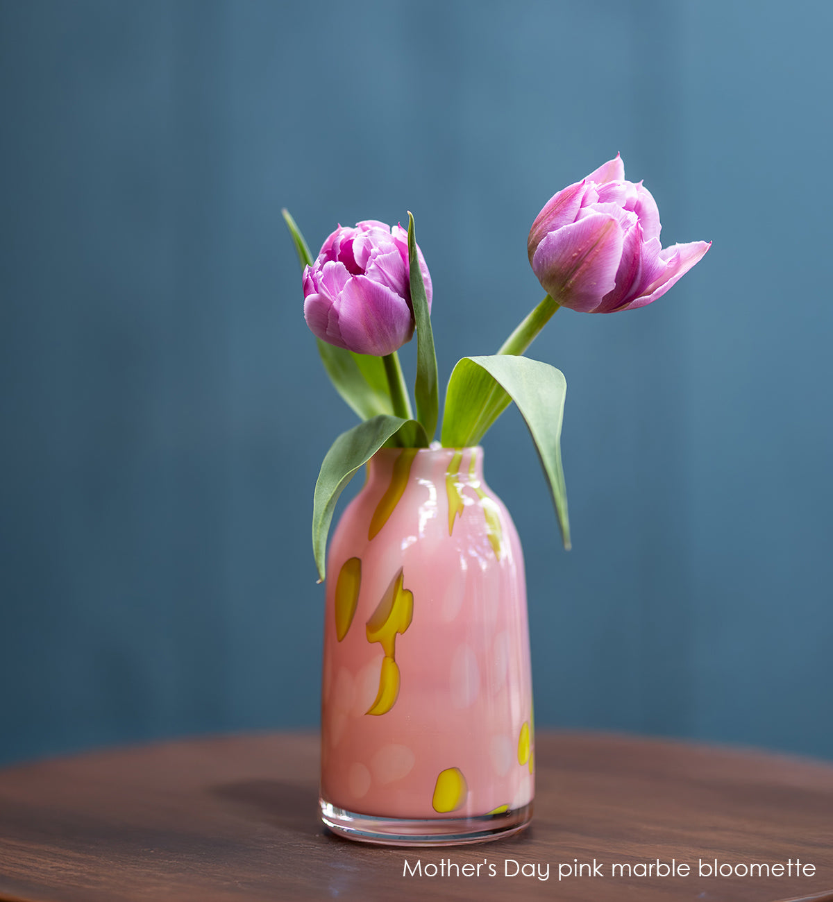 Pink marble-patterned vase with two pink tulips on a wooden surface and blue background