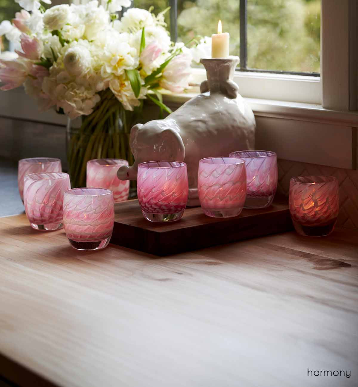 harmony, pink feathered texture hand-blown glass votive candle holder. In a lit kitchen display adorned with a ceramic elephant and a white bouquet.