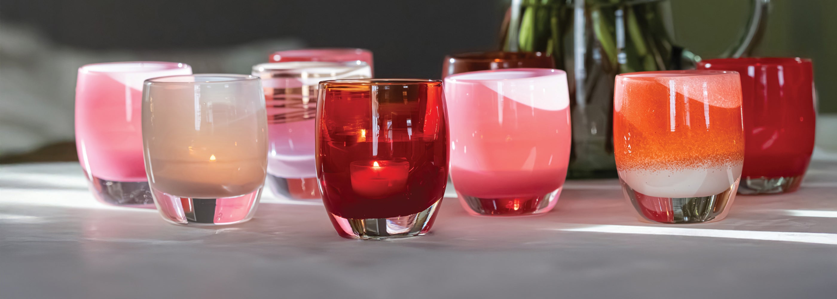 group of glass candle holders with Valentine's Day colored candles on a reflective wood surface.