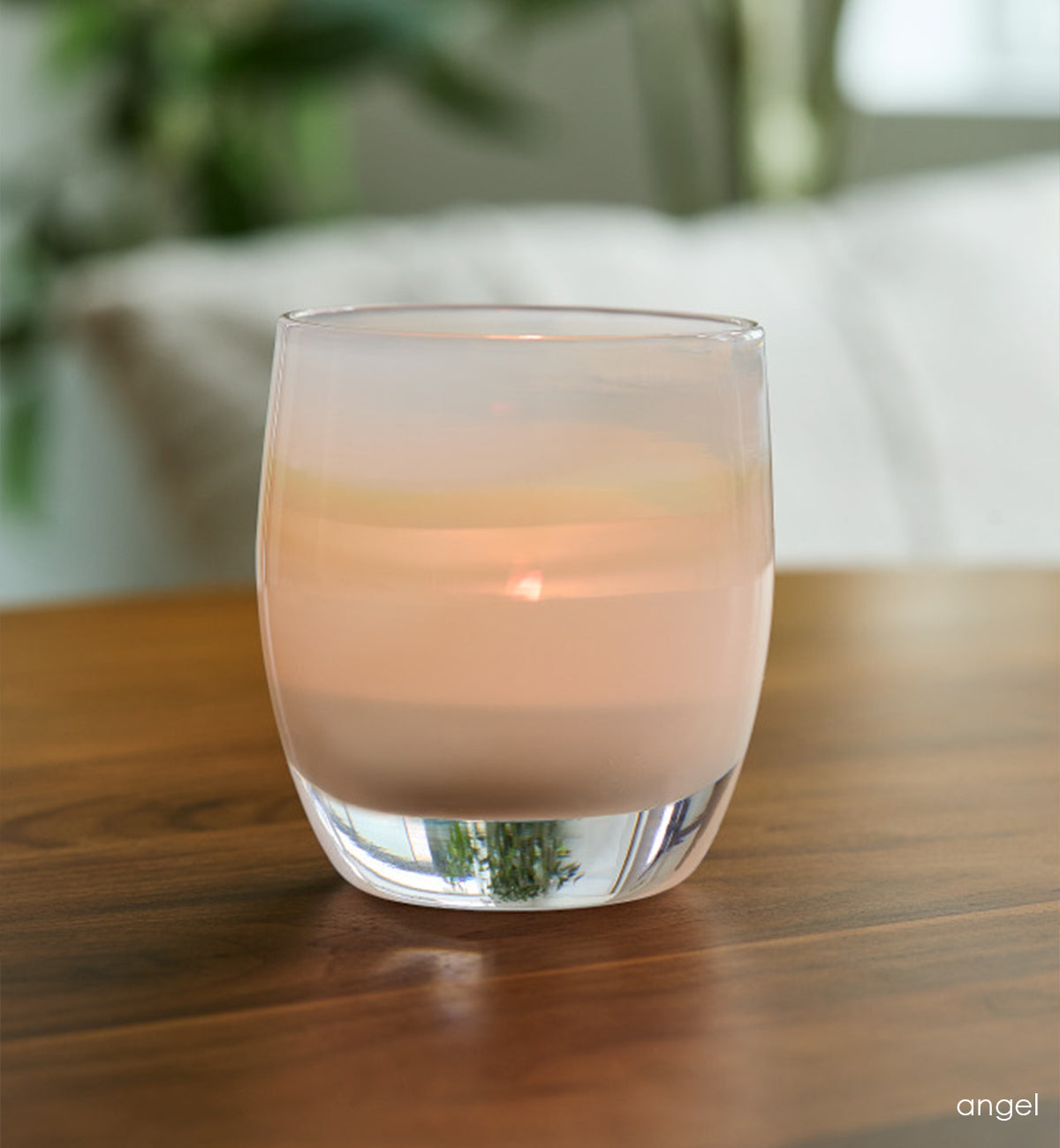 angel light yellow, hand-blown glass votive candle holder on a wood table with cushion and plant blurred in background.
