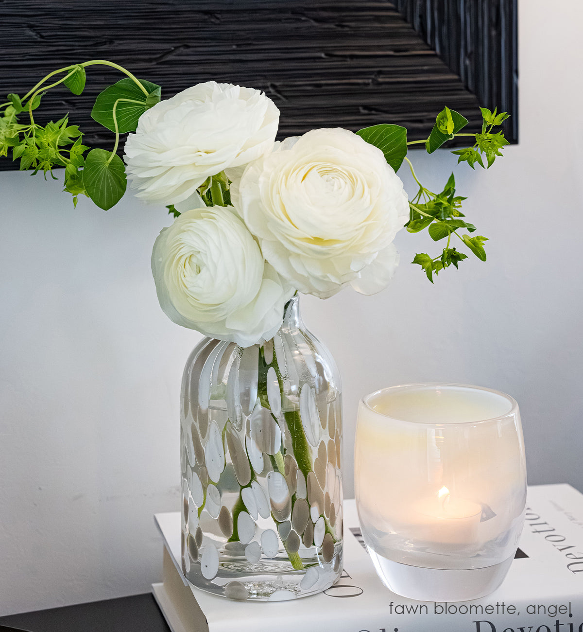 clear bloomette vase with white and tan specs holding a bouquet of white and yellow flowers on a dark surface.
