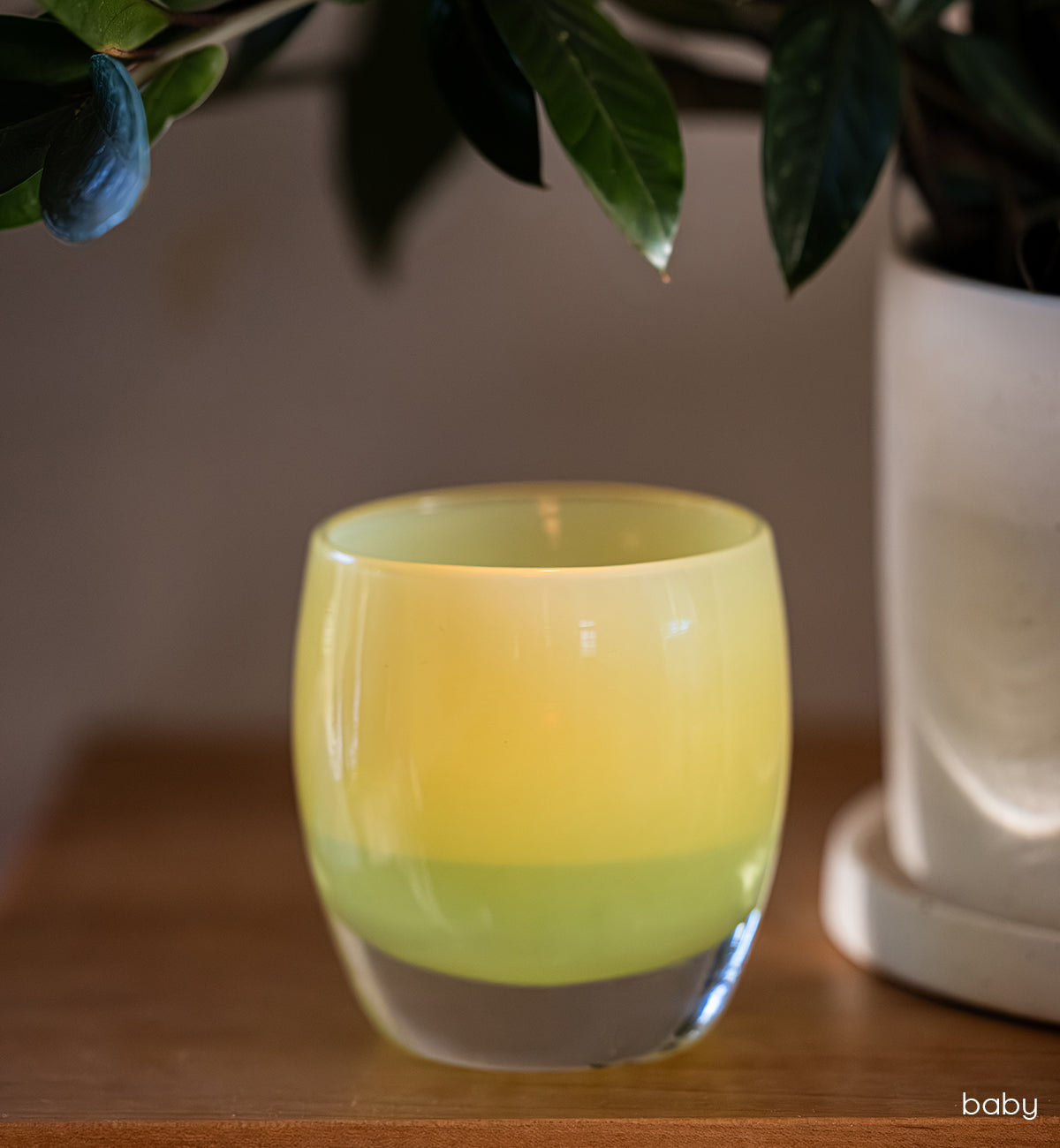 light green glass candle holder on a wooden surface with a plant in the background