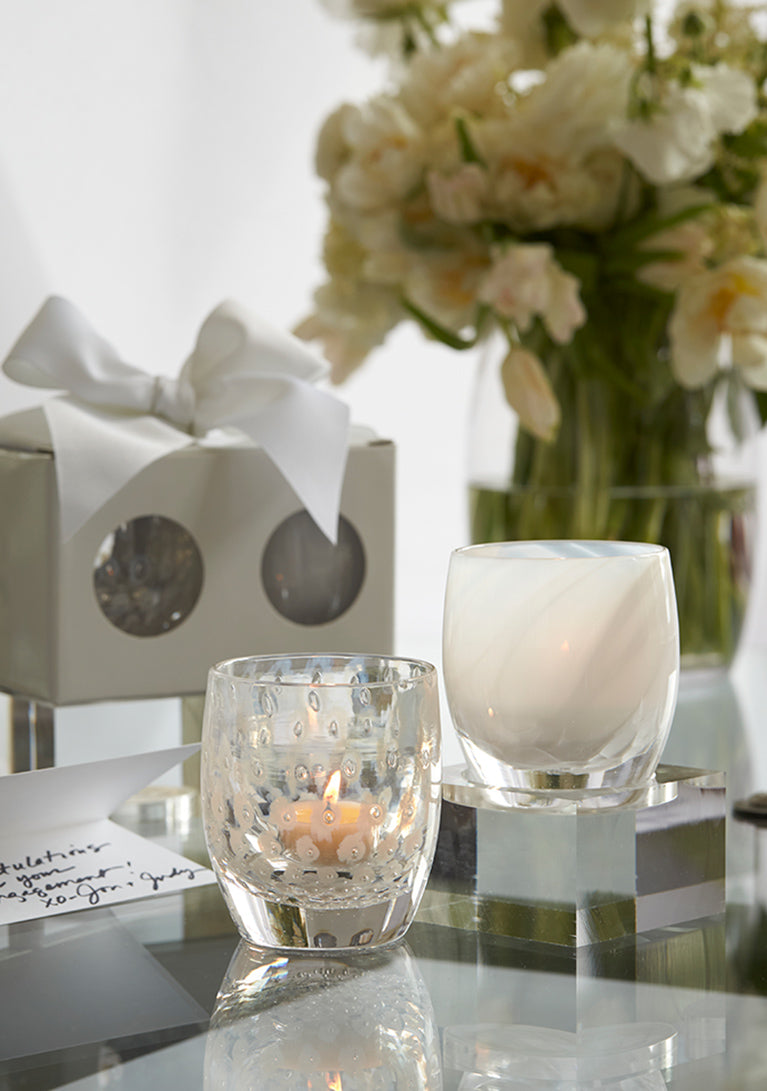 become one set on a glass table with flowers, next to a bowed box and hand written card.