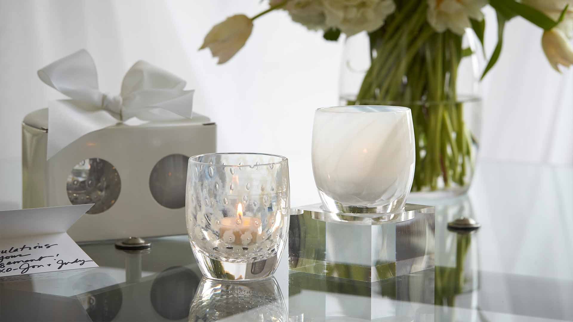 become one set on a glass table with flowers, next to a bowed box and hand written card.