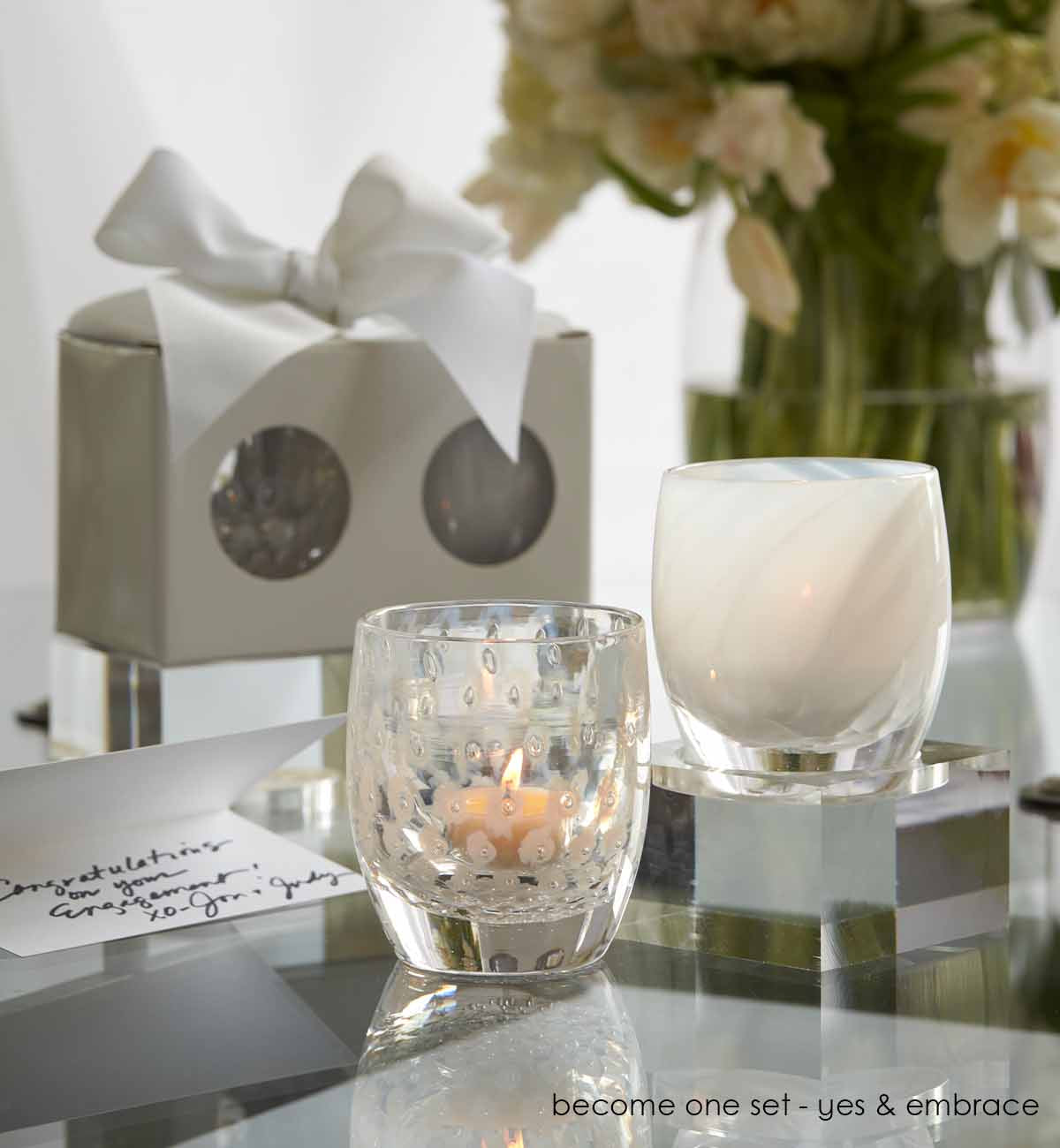 become one set on a glass table with flowers, next to a bowed box and hand written card.