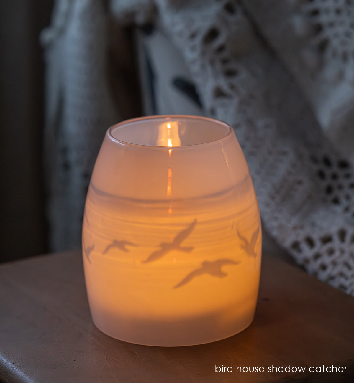 glass candle holder with bird silhouette design on a wooden surface.