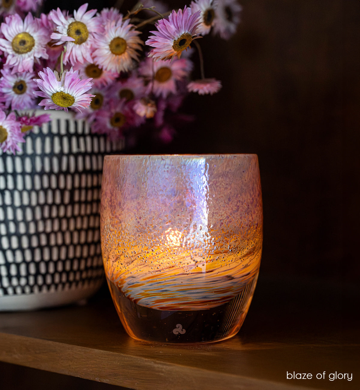 blaze of glory, metallic hand-crafted glass votive candle holder on self with a black and white vase with pink flowers. 