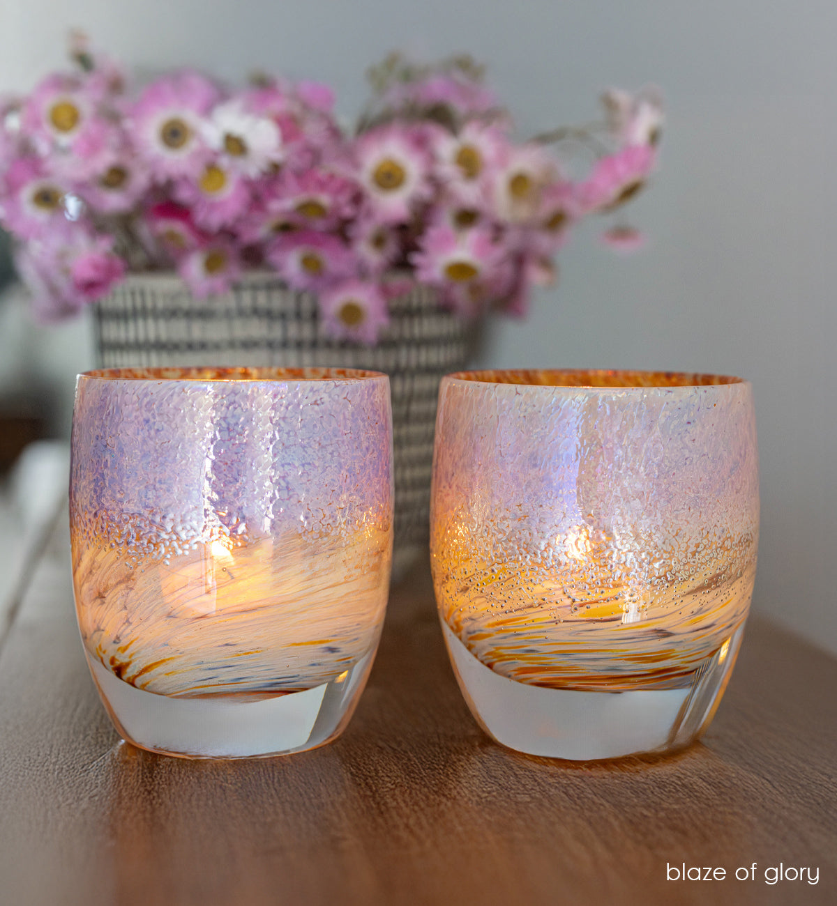 two blaze of glory, metallic hand-crafted glass votive candle holders on self with a black and white vase with pink flowers. 