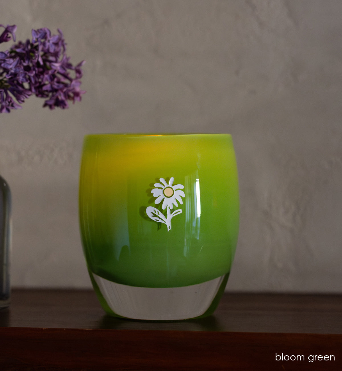 bloom green glassybaby with white flower etched on it sitting on wood shelf