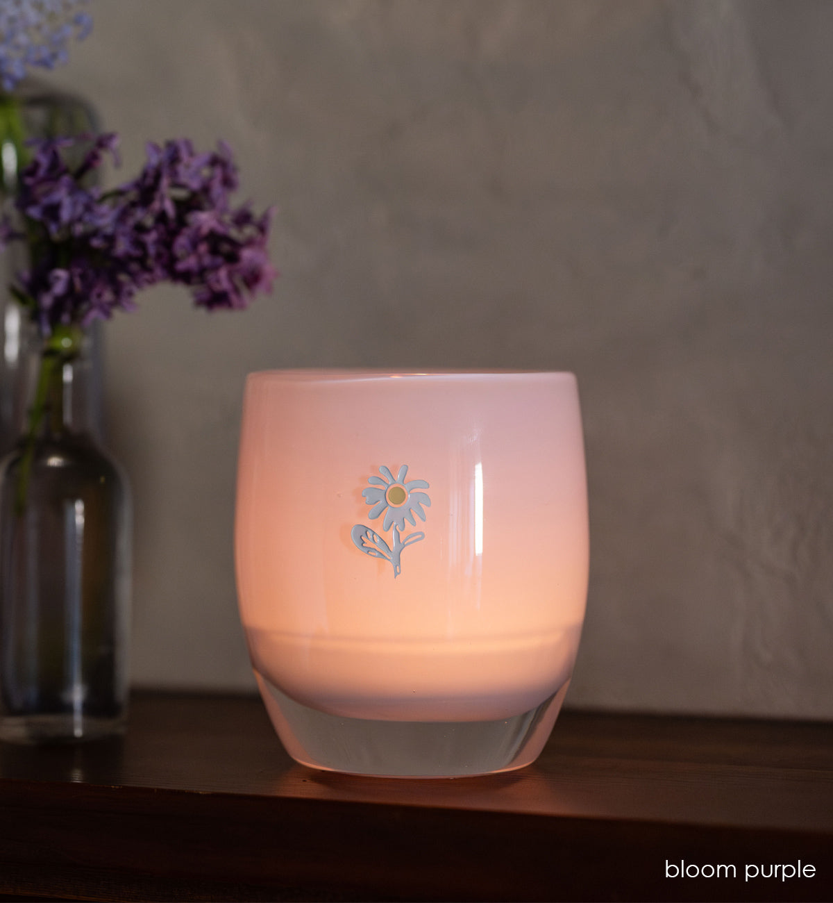 bloom purple glassybaby with white flower etched on it sitting on wood shelf. 