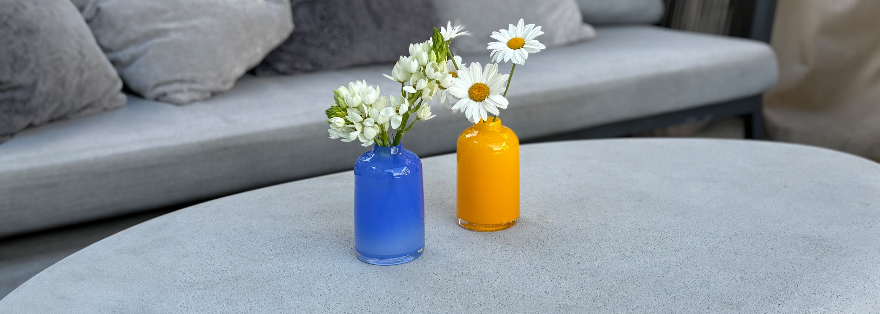 french blue bloomette and marigold bloomette with white flowers on gray table in front of gray couch.