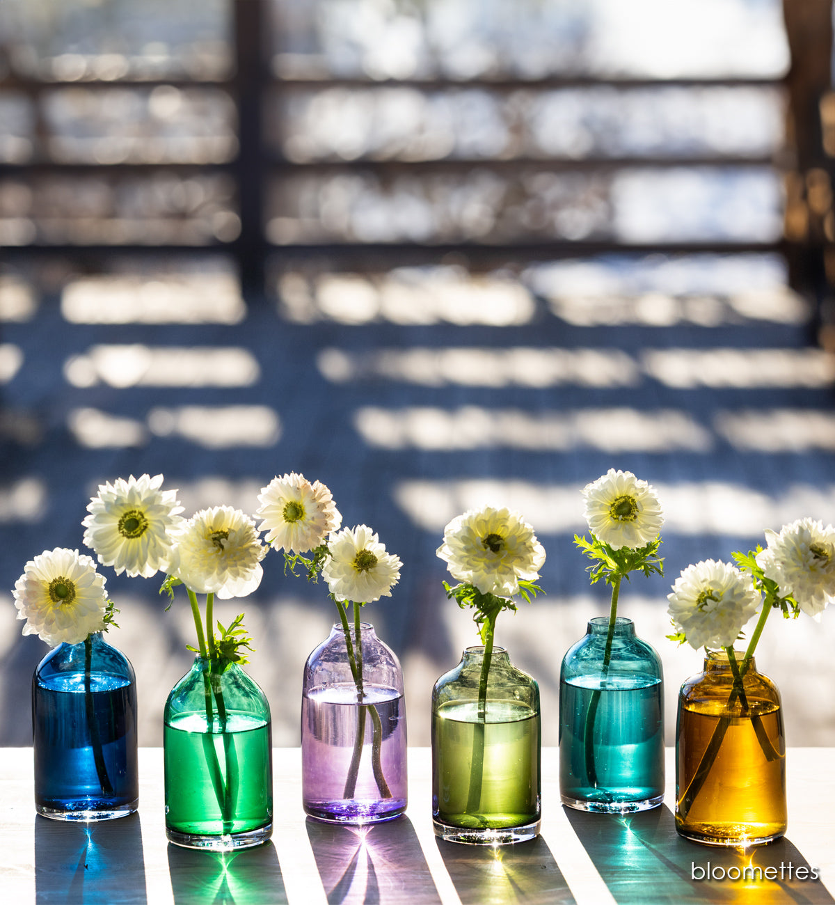 hand-blown glass flower bud vases with white flowers on wood table outside