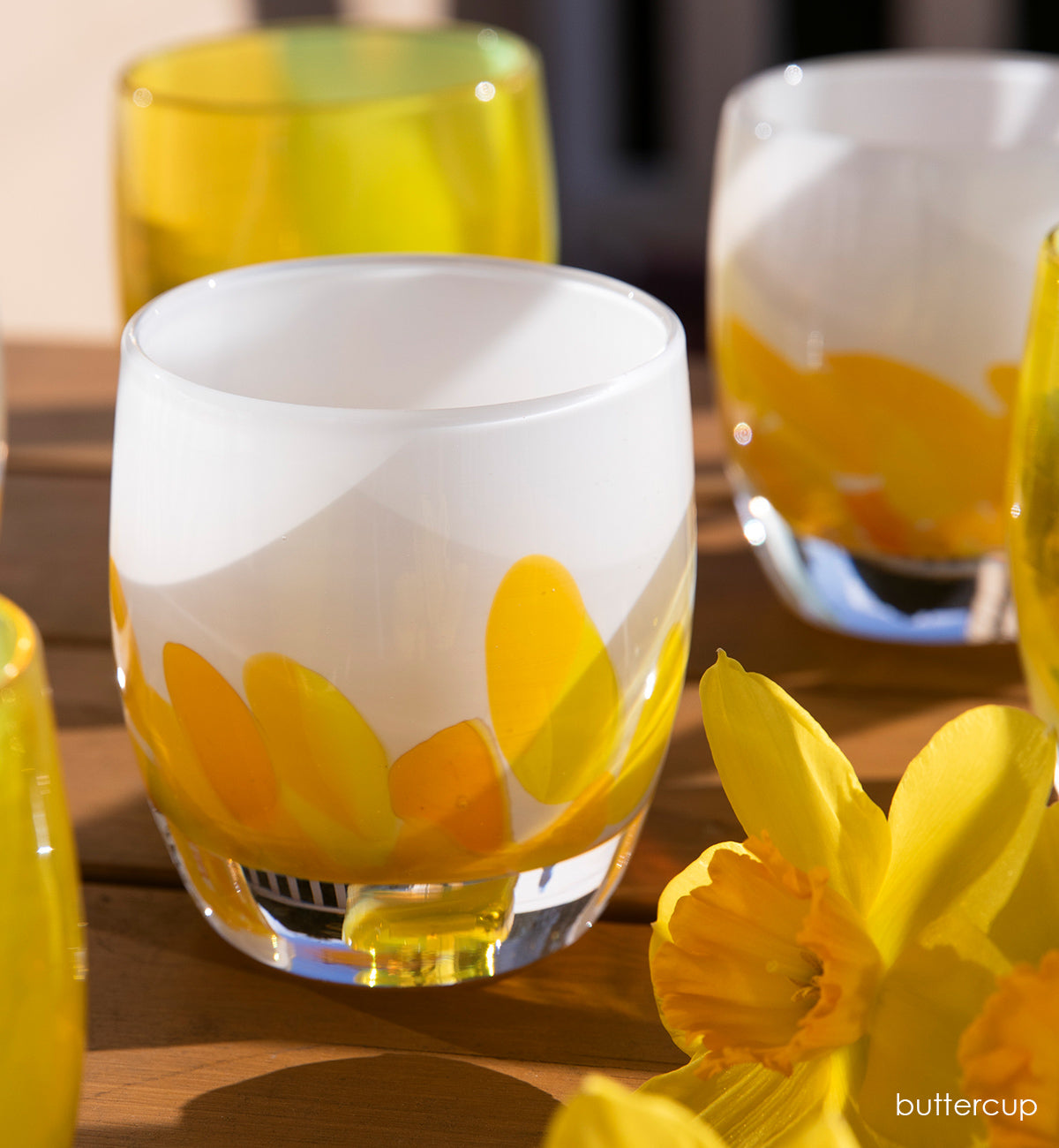 buttercup, yellow petals on white, hand-blown glass votive candle holders on a wood table with fresh daffodil flowers.
