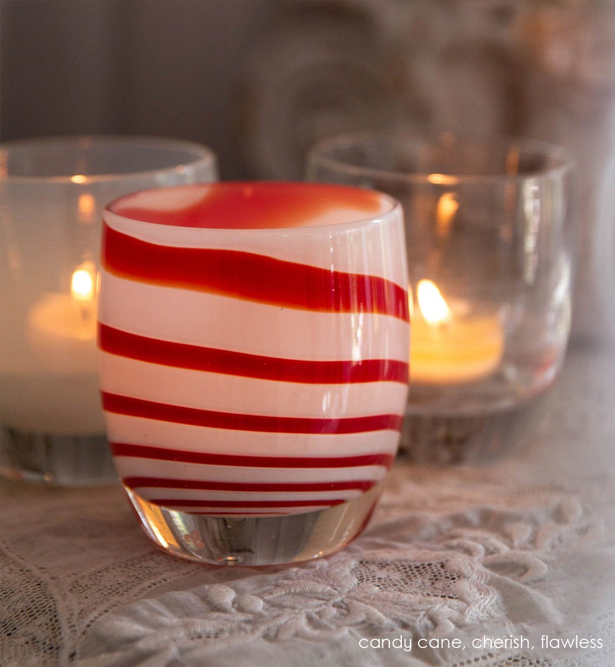 candy cane, red and white striped, hand-blown glass votive candle holder. Paired with dream and flawless on a lace tablecloth.